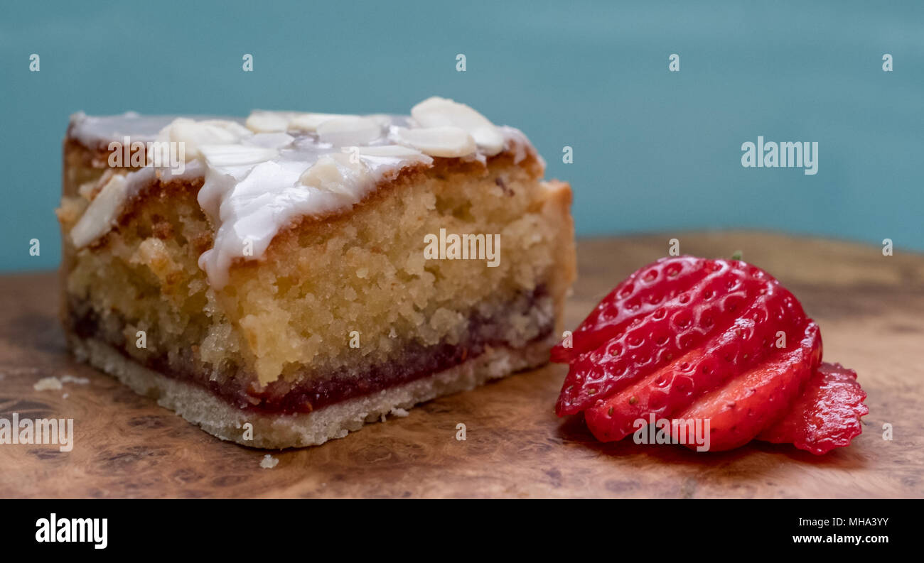 Slice of bakewell tart cake on olive wood platter with aqua blue