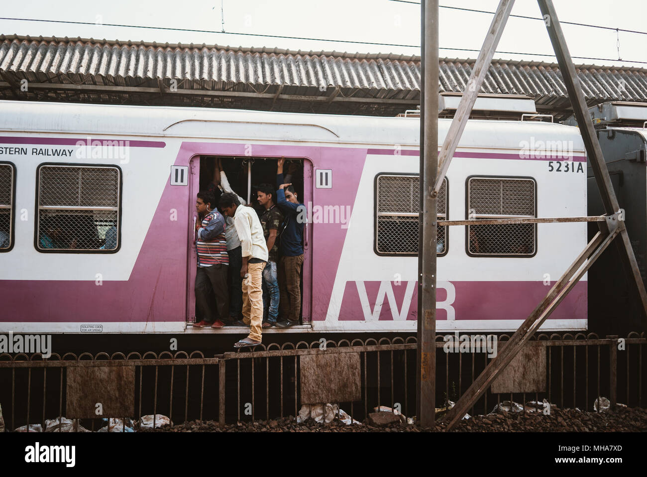 men with their feet hanging out of a pink train heading to the city in Mumbai, India Stock Photo