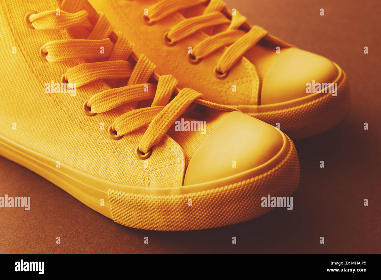 Brand new yellow sneakers on the floor, retro toned youth lifestyle footwear concept Stock Photo