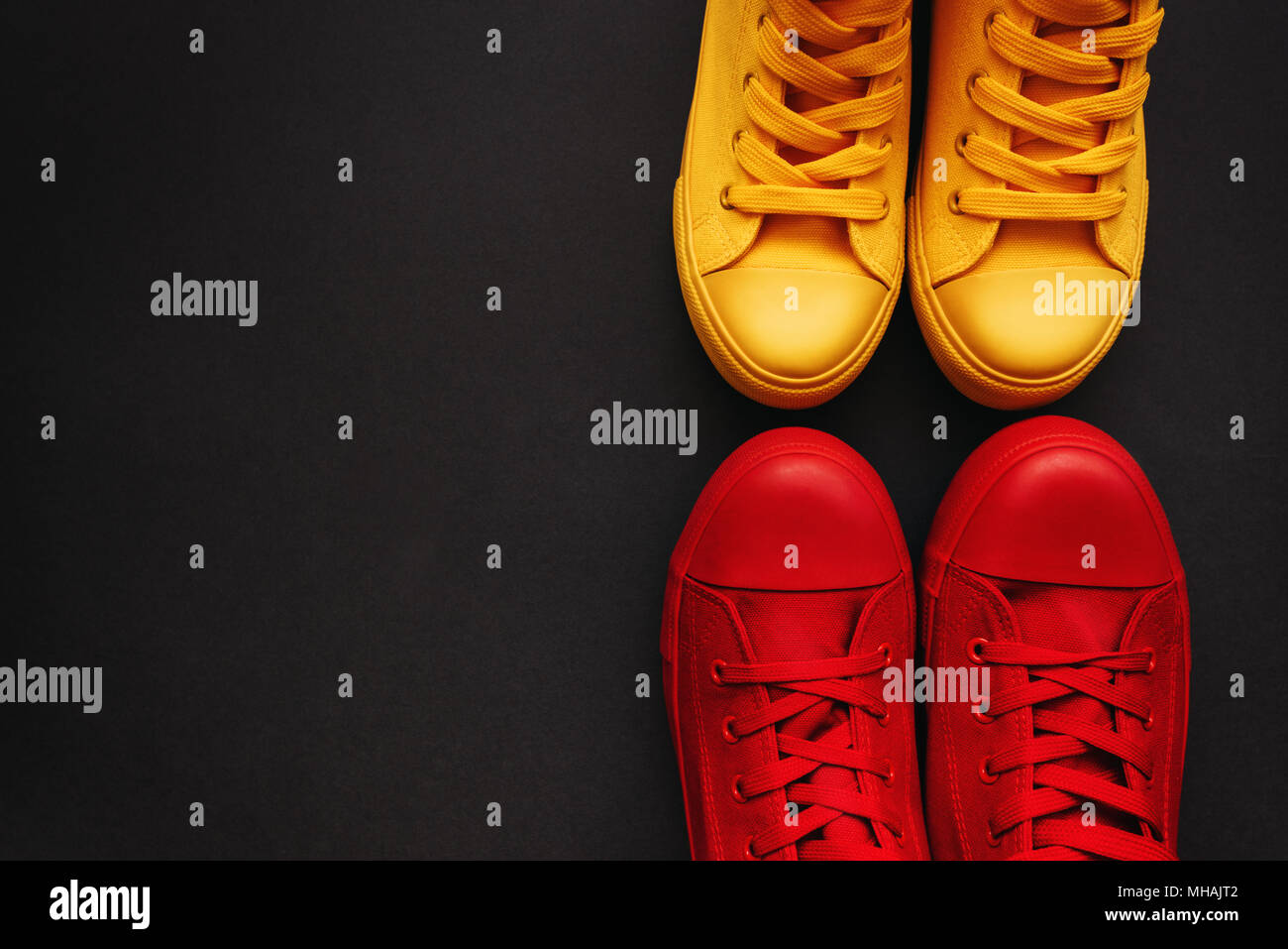 Young adult people on a love date, conceptual image. Top view of two pair of casual sneakers, yellow and red, from above Stock Photo