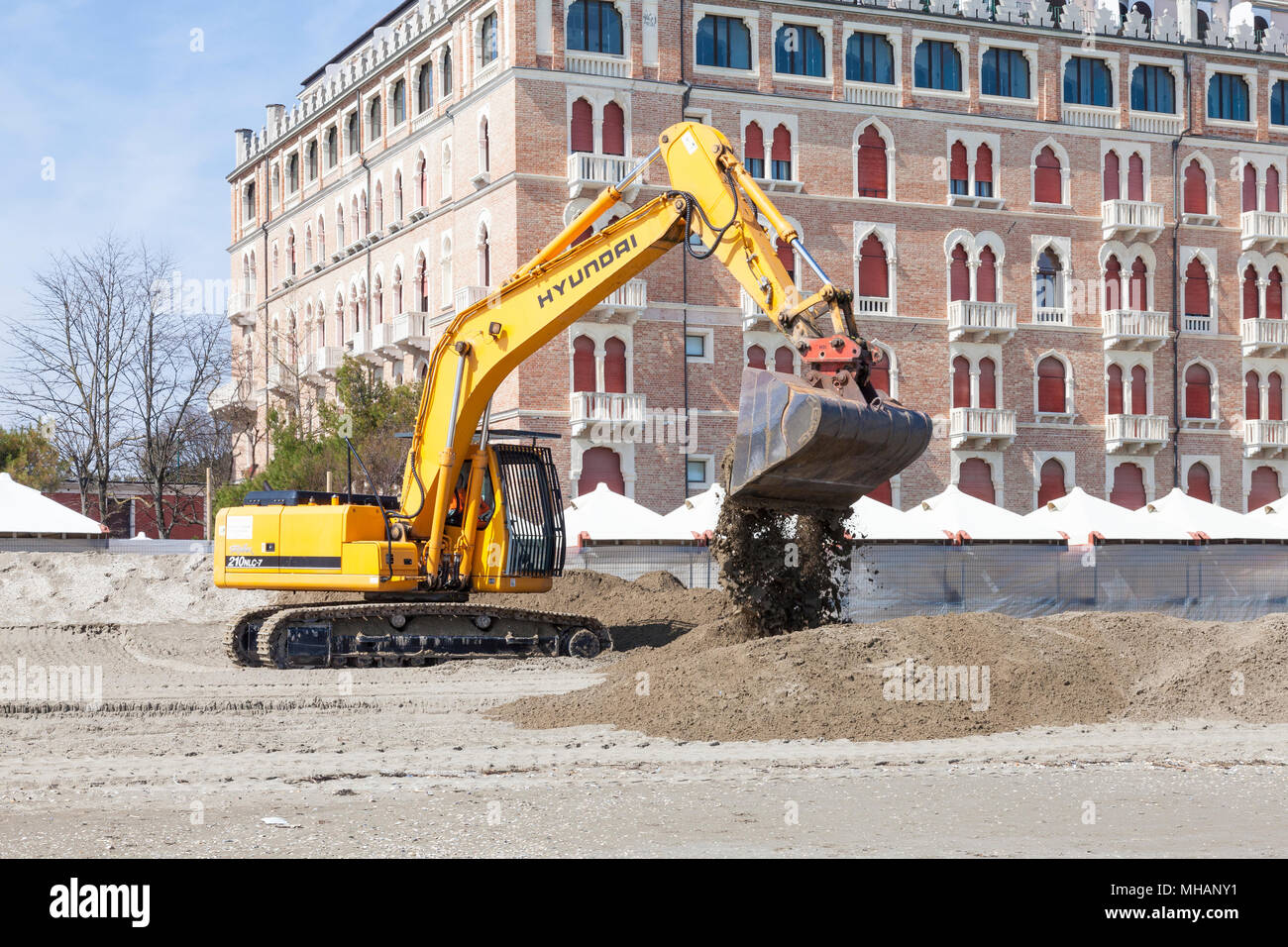 Excavator (digger) moving sand on the beach at Lido di Venezia , Venice,  Veneto, Italy in front of the Excelsior Hotel preparing it for the summer se Stock Photo