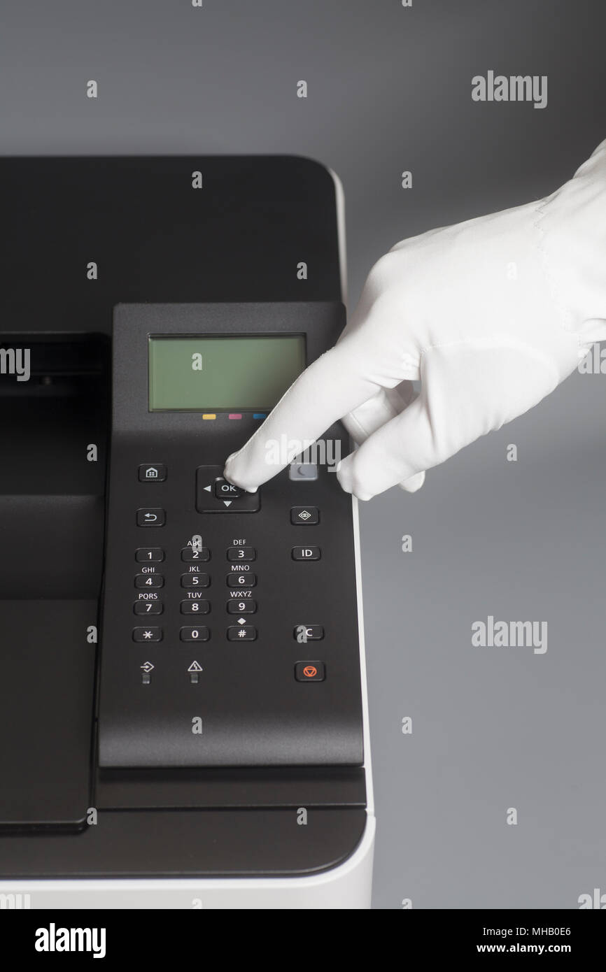 Woman's hands in white glove pressing button on control panel color laser printer on gray Stock Photo