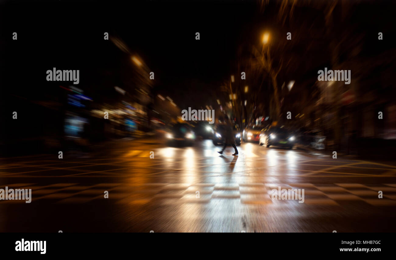 Blurry motion image of man crossing a street at night in Paris. Cars wait at traffic lights. Stock Photo