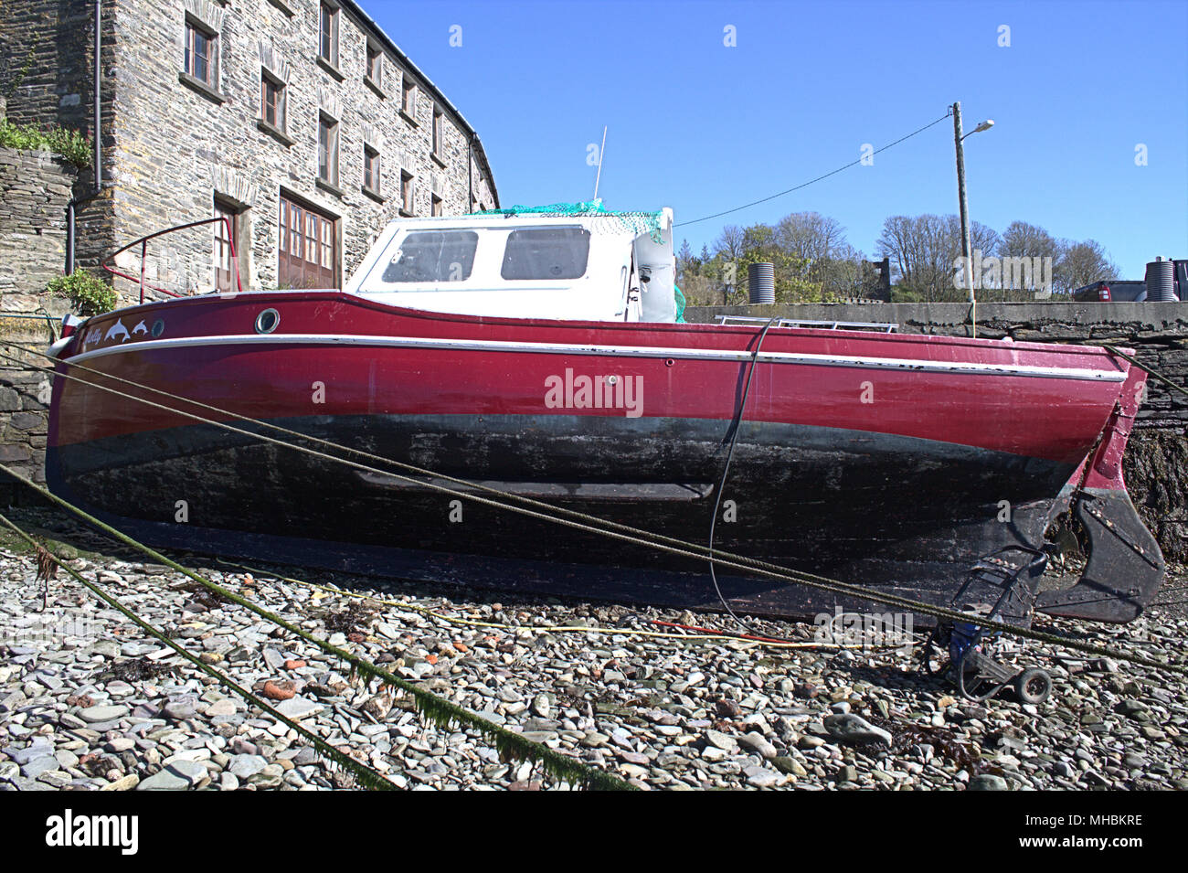 classic wooden hulled boat with enclosed wheel house, built for leisure fishing moored up alongside a harbour wall at low tide being repainted. Stock Photo