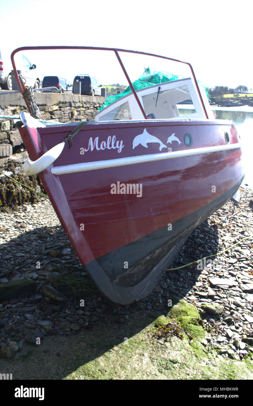 classic wooden hulled boat with enclosed wheel house, built for leisure fishing moored up alongside a harbour wall at low tide being repainted. Stock Photo