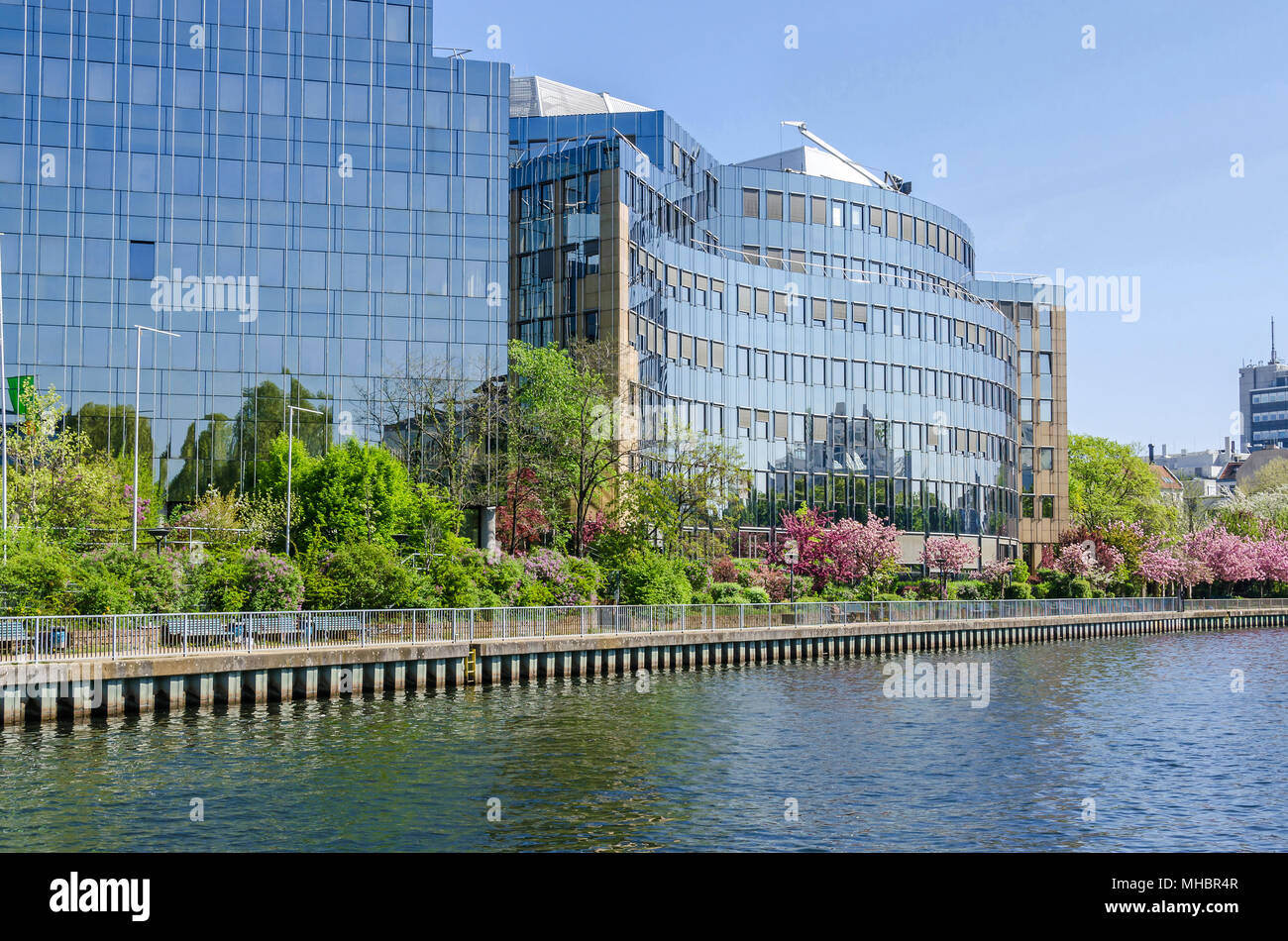 Reflecting facade of the buildings of Skandia insurance company on banks of the river Spree in Berlin with flowering trees in the springtime Stock Photo