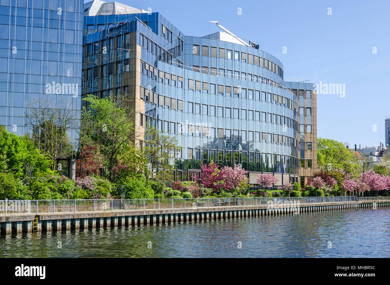 Reflecting facade of the buildings of Skandia insurance company on banks of the river Spree in Berlin with flowering trees in the springtime Stock Photo
