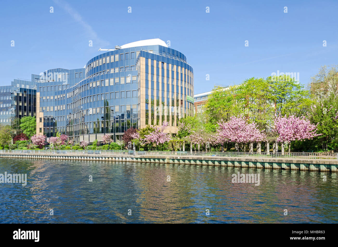 Reflecting facade of the buildings of Skandia insurance company on banks of the river Spree in Berlin with flowering trees in the springtime Stock Photo