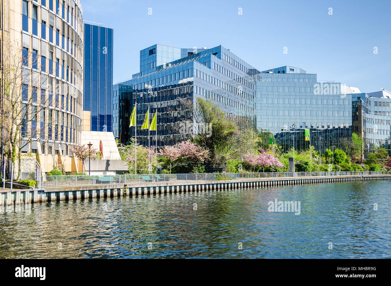 Banks of the river Spree with the reflecting facade of the buildings of Skandia insurance company and flowering trees in the springtime in Berlin Stock Photo