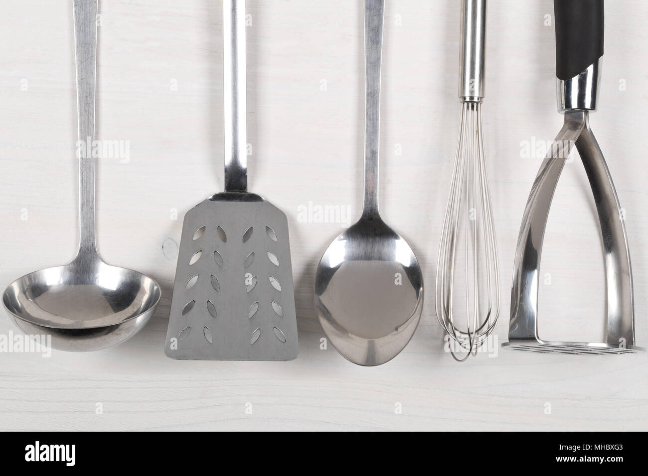 https://c8.alamy.com/comp/MHBXG3/row-of-metal-kitchen-tools-with-spoons-and-spatulas-from-above-on-white-wooden-board-background-MHBXG3.jpg