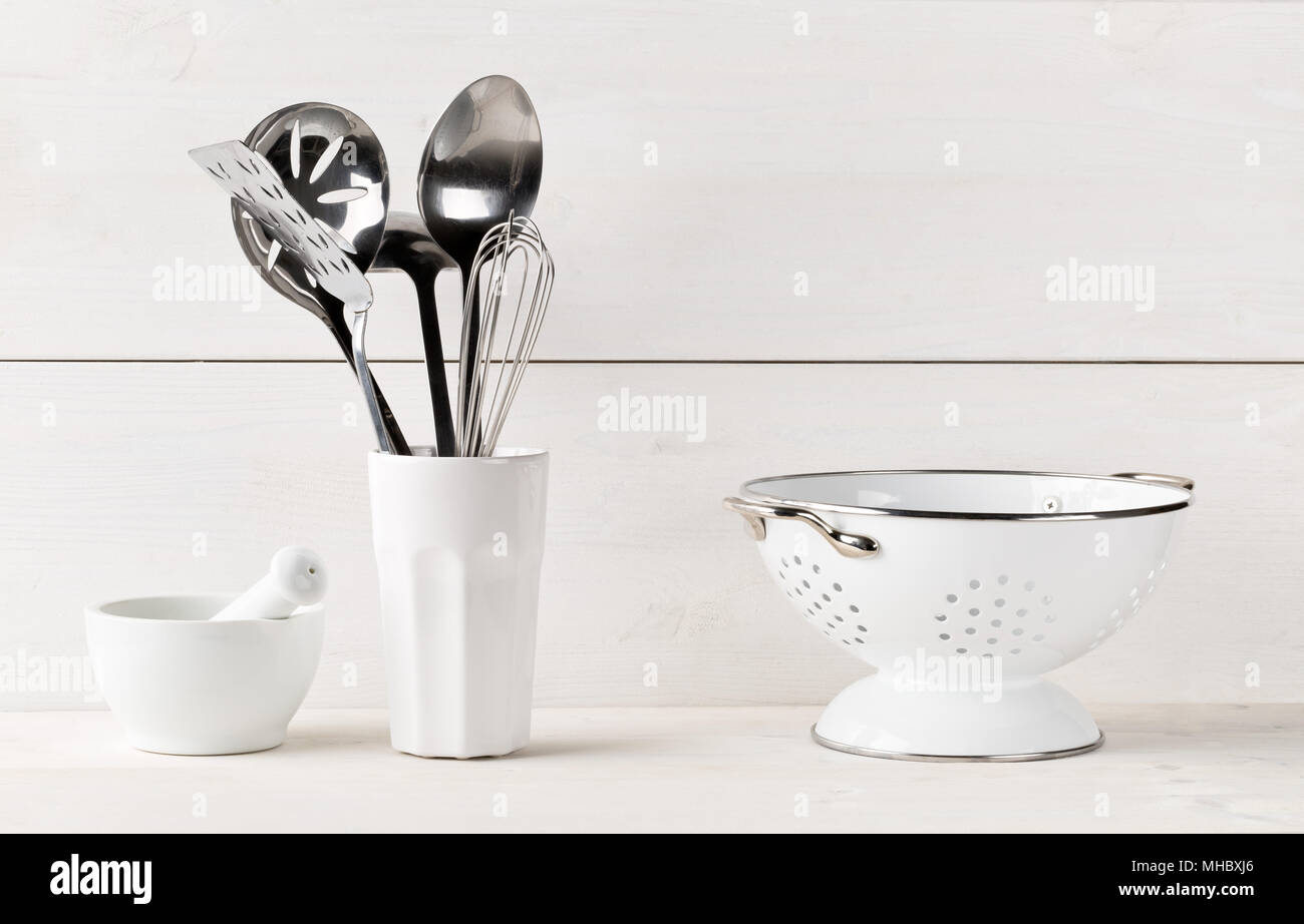 Kitchen cooking utensils in white cup with pestle and mortar and sieve on white table with white