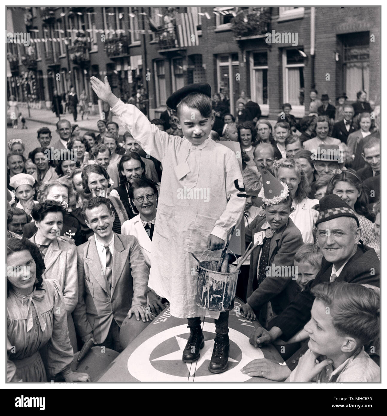 HITLER PARODY at end of World War II.. Dutch street festivities after the liberation in the capital of Holland Amsterdam.. Little boy dressed as an artist painter Adolf Hitler gives the Heil Hitler salute in parody June 28, 1945 WW2 is at an end Stock Photo
