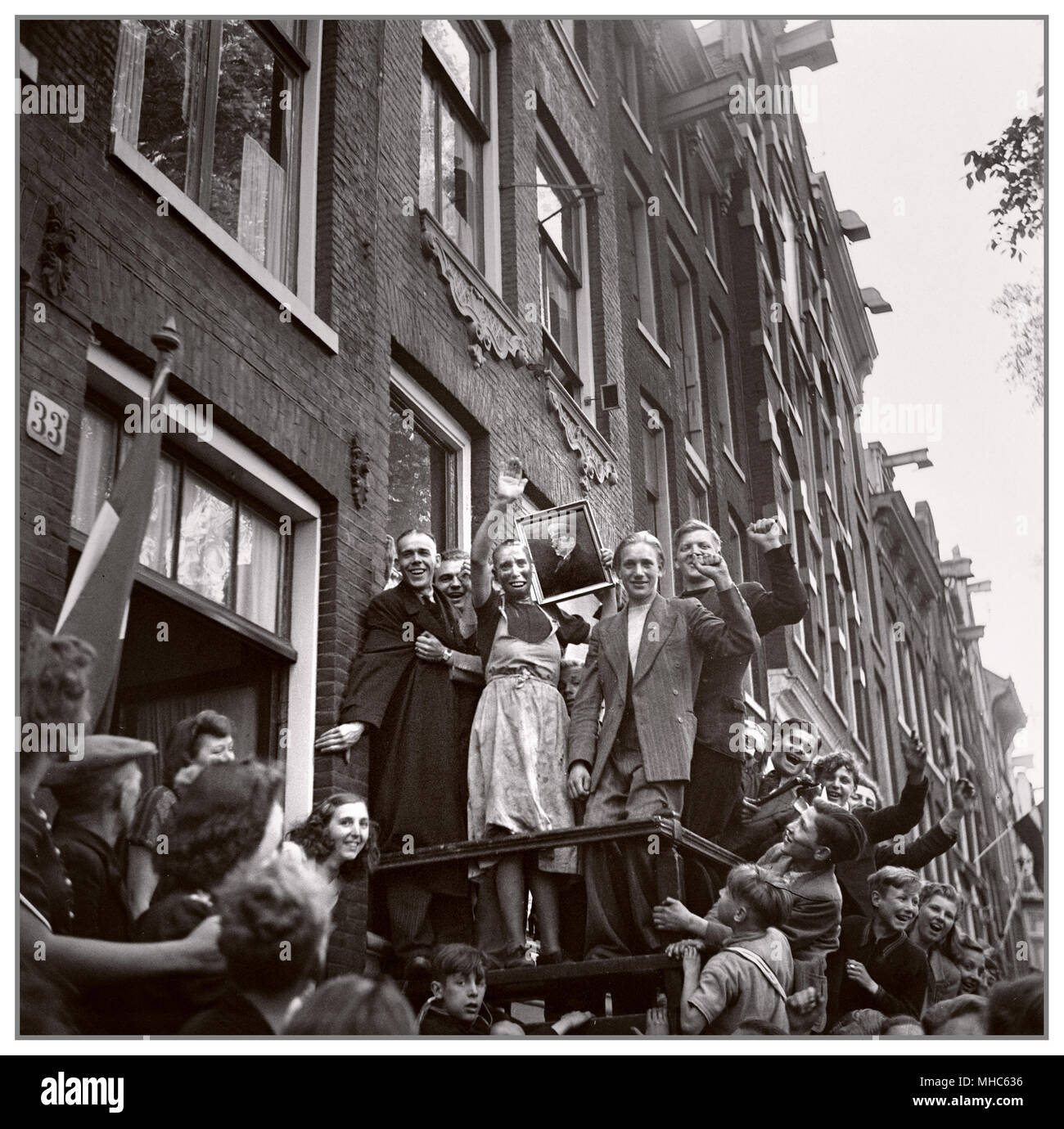 Een kaalgeschoren vrouw, verdacht van collaboratie, wordt publiekelijk gedwongen het portret van Hitler te groeten. Scheveningen (Nederland), mei 1945. Vrouwen die omgingen met Duitse soldaten werden wel 'moffenmeid' of 'moffenhoer' genoemd. DateMay 1945 Stock Photo