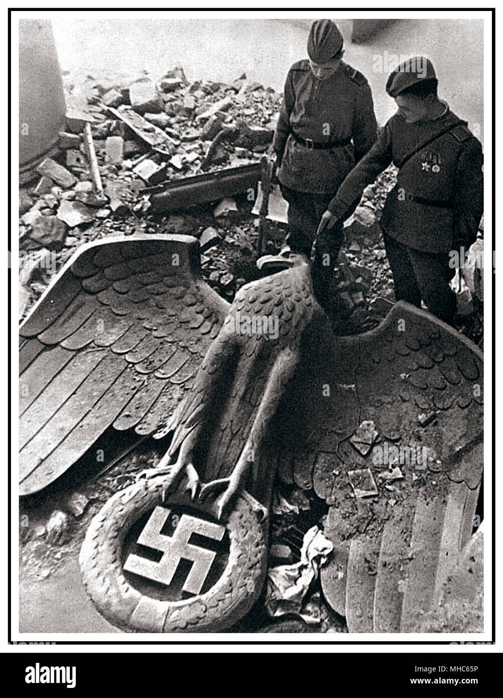 FALL OF BERLIN AND THE THIRD  REICH 1945 WW2 in Europe ends.. Russian soldiers after the fall of Berlin looking at a torn down German Nazi Eagle with Swastika emblem lying in the ruins of former seat of Nazi Germany power, The Reich Chancellery Berlin Germany  'The Fall of The Third Reich' 8 May 1945 World War II Stock Photo