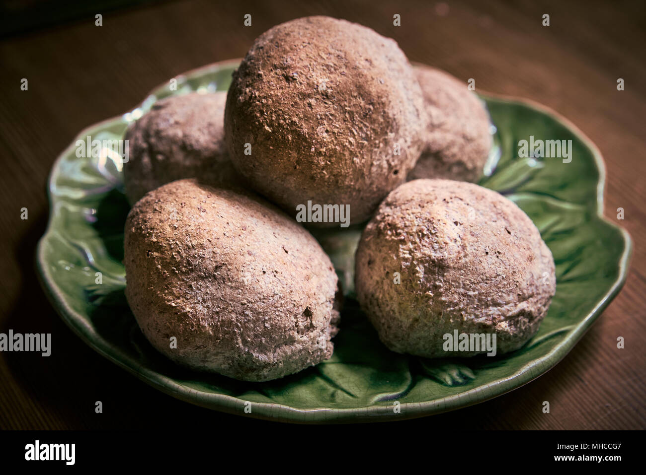 Rustic wholemeal rolls on a green serving plate Stock Photo