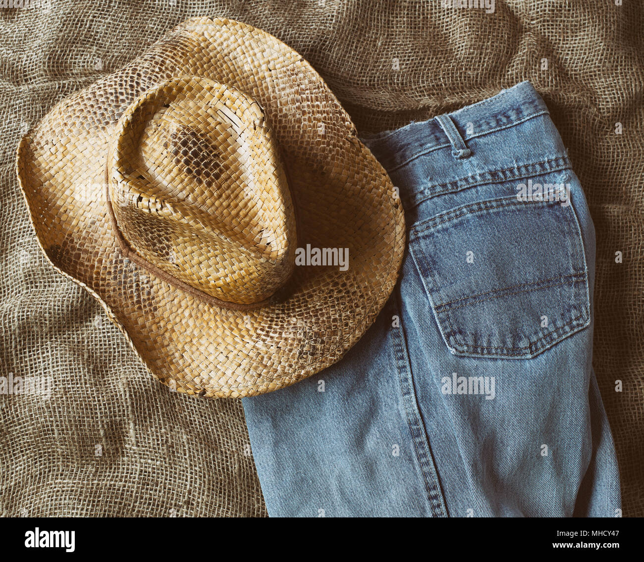 Straw hat and faded blue jeans on burlap. Top down view. Stock Photo