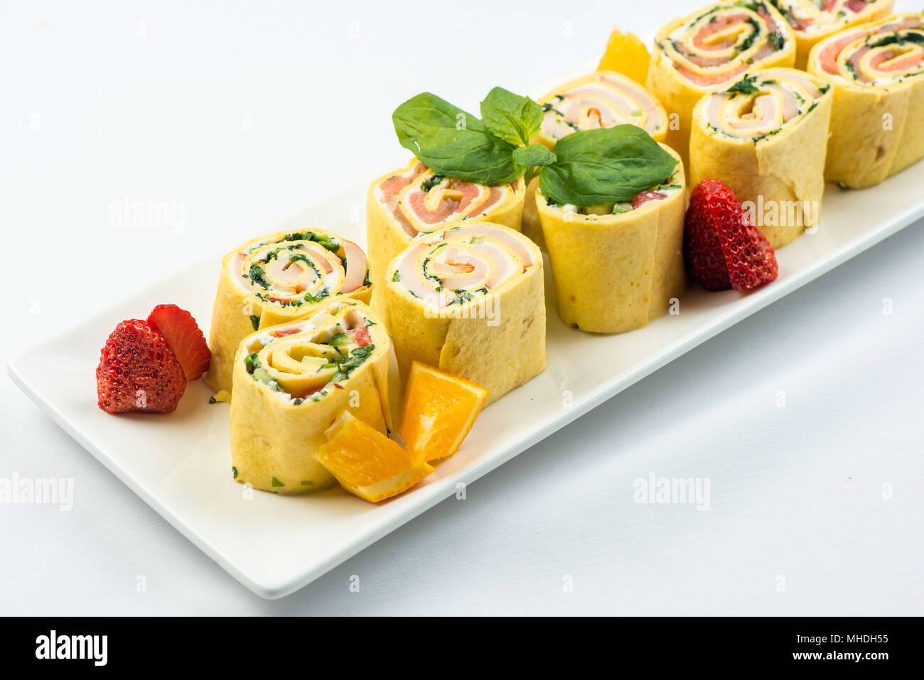 Rolls of thin pancakes with smoked salmon, horseradish cream cheese and rocket leaves on white