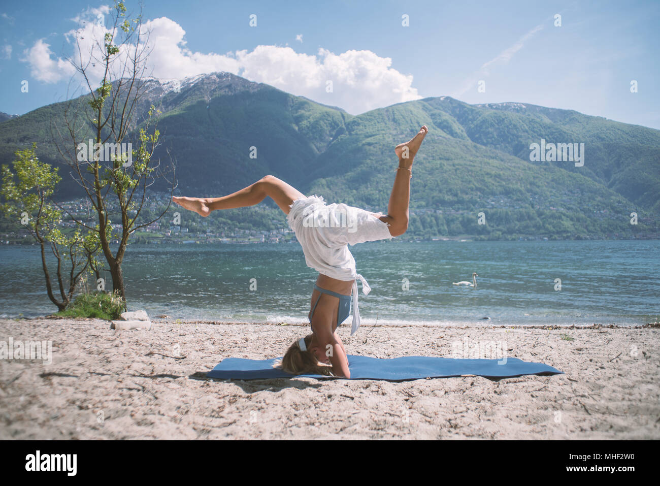 Young woman exercising yoga by the lake and mountains, shot in Ticino Canton, Switzerland, Europe. People relaxation wellbeing concept Stock Photo