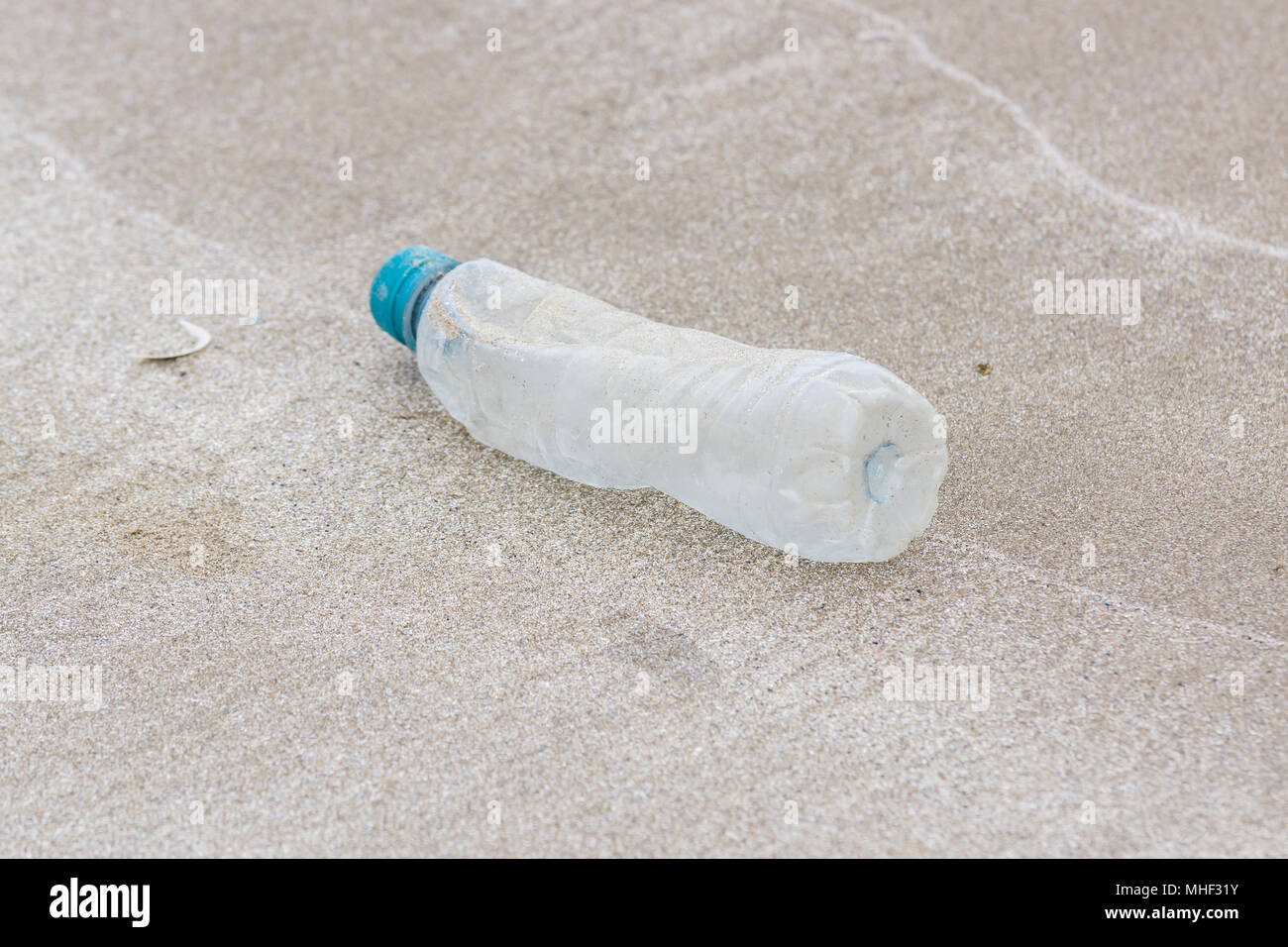 Plastic drink bottle washed up on a sandy beach an example of the many pieces of garbage in the sea around the world Stock Photo