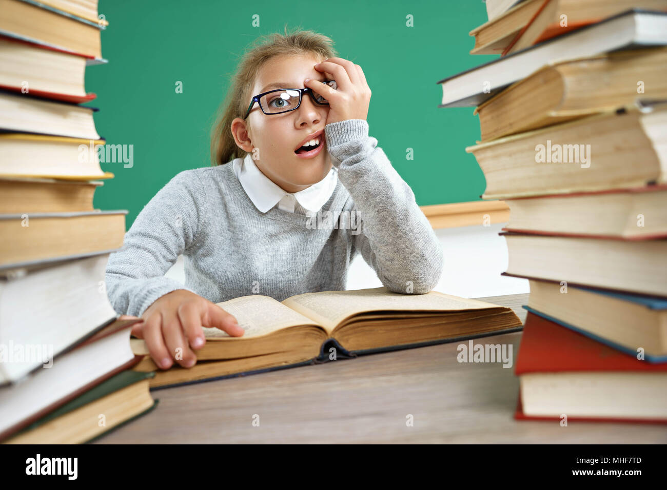Exhausted or bored schoolgirl around a lots of books. Photo of little girl in classroom. Education concept Stock Photo