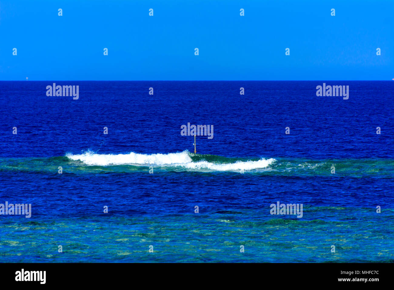 A small wave in the shallows is far from the shore against the background of the blue sky and the transparent sea off the coast of the unique Ras Moha Stock Photo