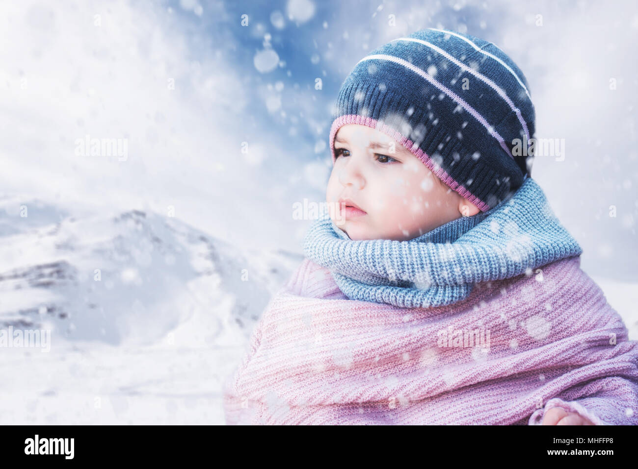 Cute baby girl wearing a warm winter hat and a colorful hat on a snowy background Stock Photo