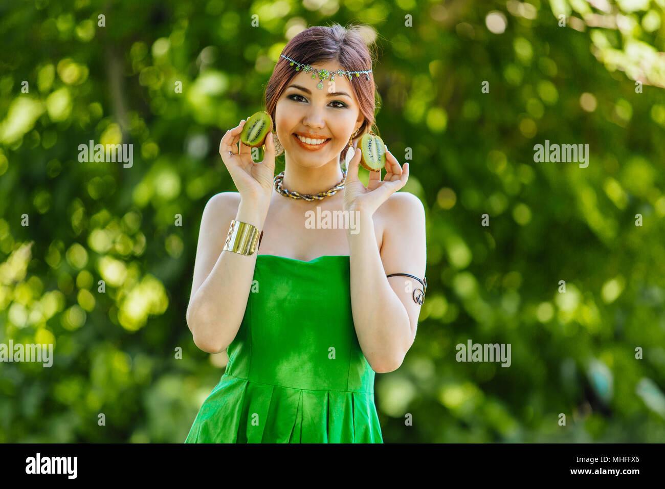Portrait of a beautiful young asian woman holding two halves of kiwi ...