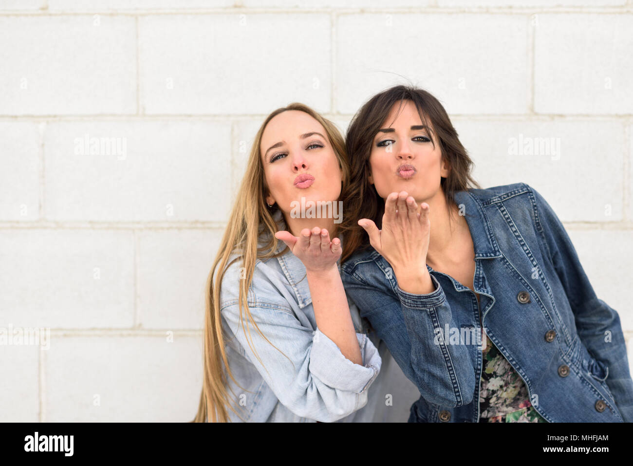 Two young women blowing a kiss on urban wall outdoors. Stock Photo