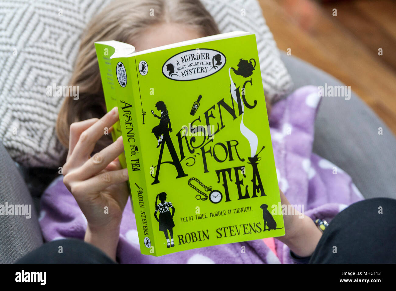 Child, girl kid, reading a murder mystery book, Arsenic for Tea, by Robin Stevens, Green Cover reading concept, bookworm, love reading Stock Photo