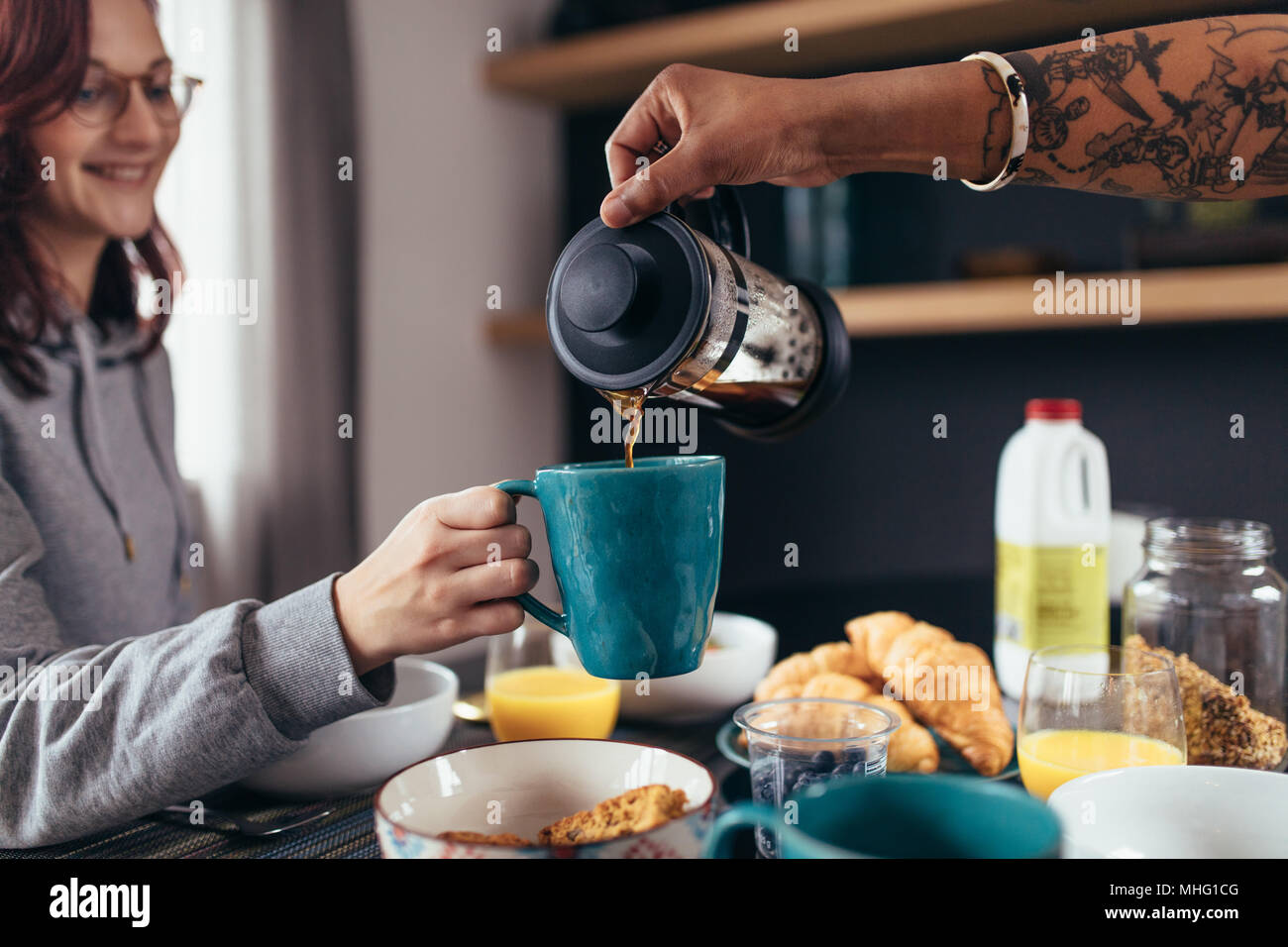 Close up of boyfriend pouring coffee into the cup of his girlfriend. Couple having breakfast together in morning. Stock Photo