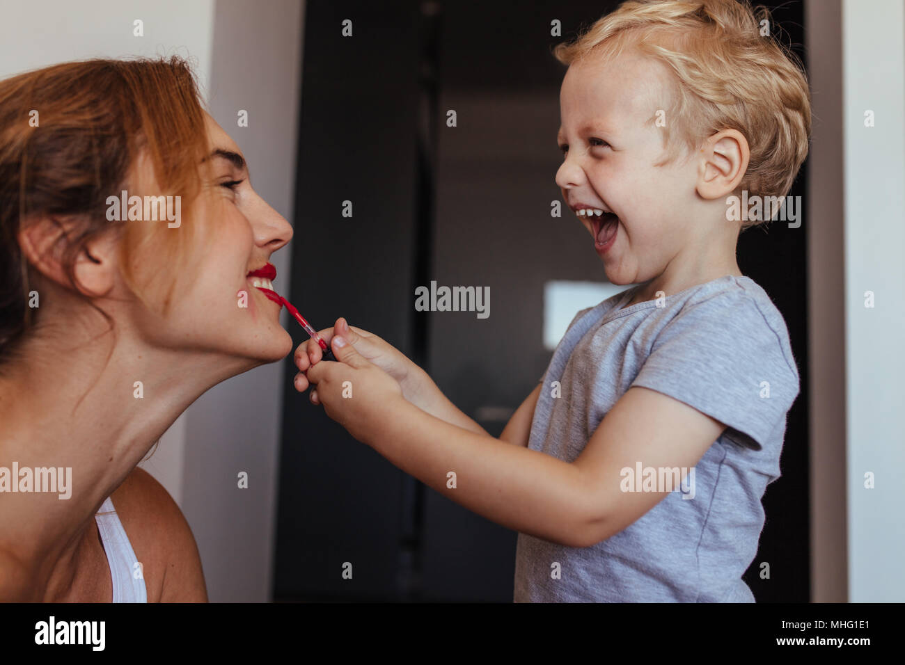 Smiling little boy putting on the makeup to her mother. Happy mother and son playing with makeup at home. Stock Photo