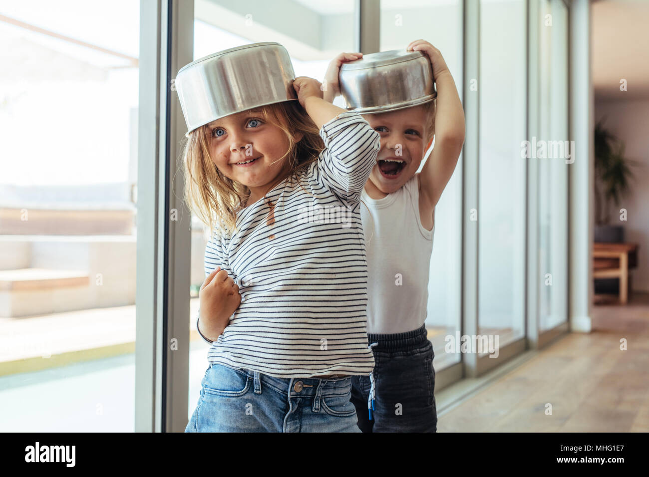 Cute little kids wearing bowl as helmet and playing at home. Children play knight with kitchen utensil. Stock Photo