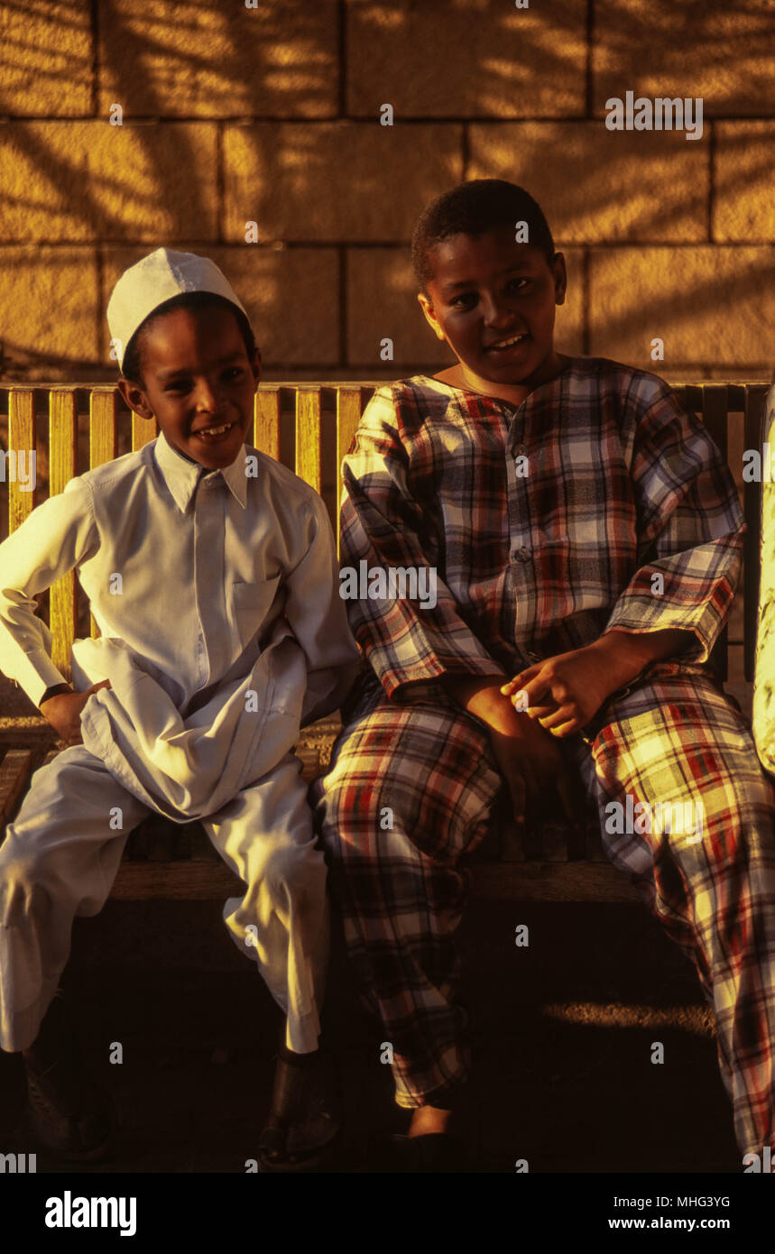 Two Saudi boys sitting on a wooden bench in Jeddah, by the red sea. Stock Photo