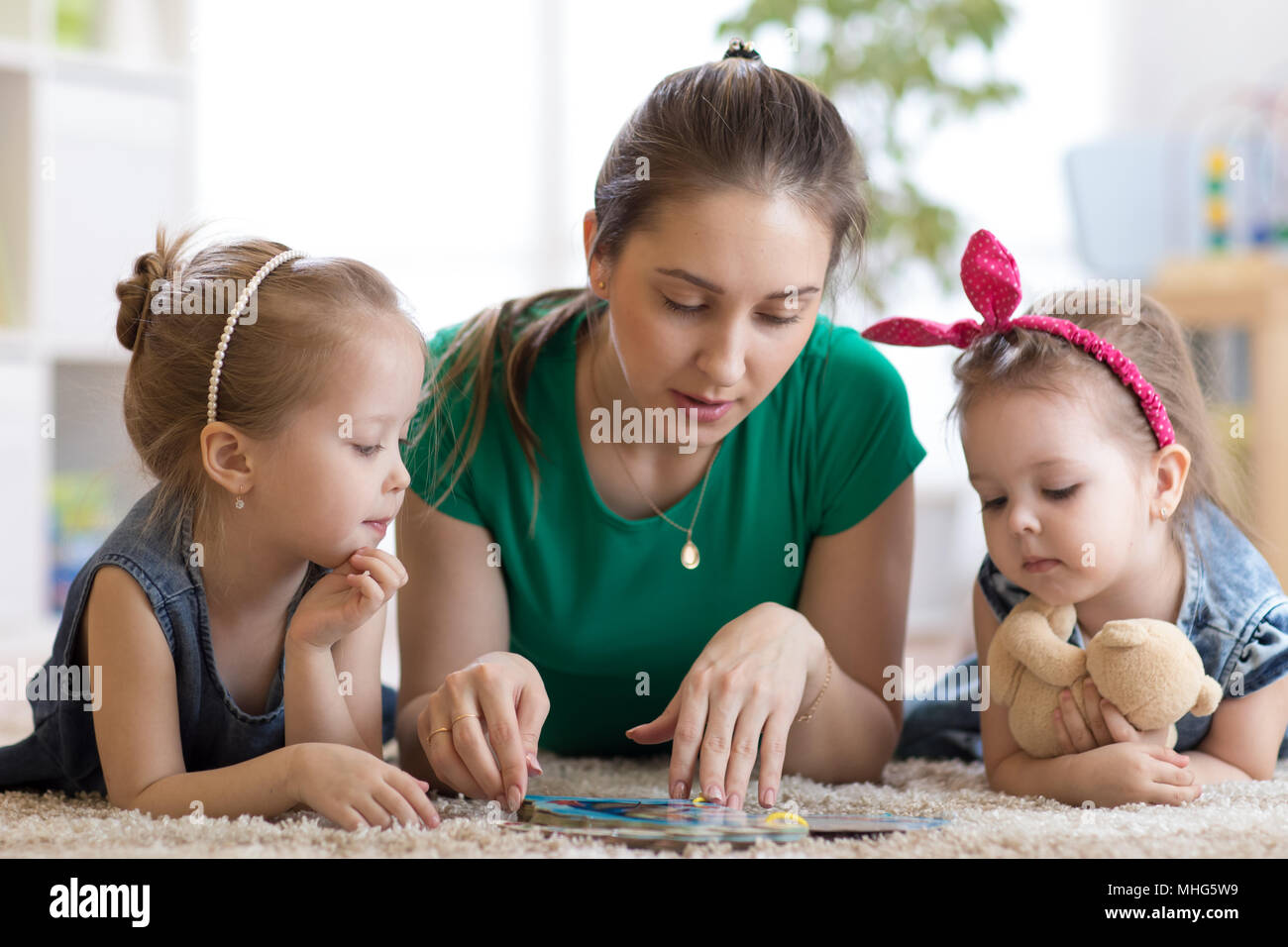 Cute mother and her two daughters children reading together Stock Photo