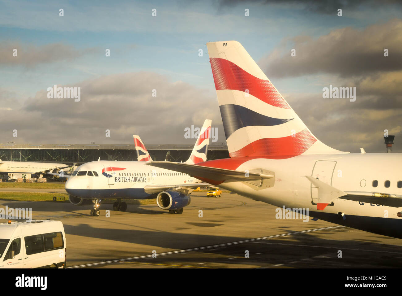 Close up of the tail of a British Airways Airbus passenger jet at London Heathrow Airport with another aircraft passing behind Stock Photo
