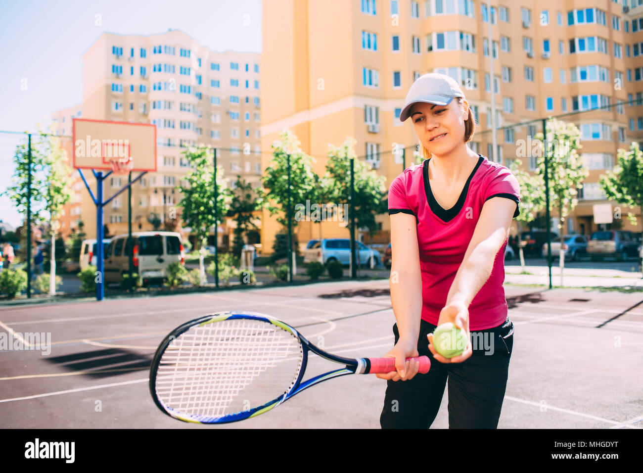 Pretty woman holding a tennis ball and racket with visor smiles on tennis tennis court on a sunny day Stock Photo