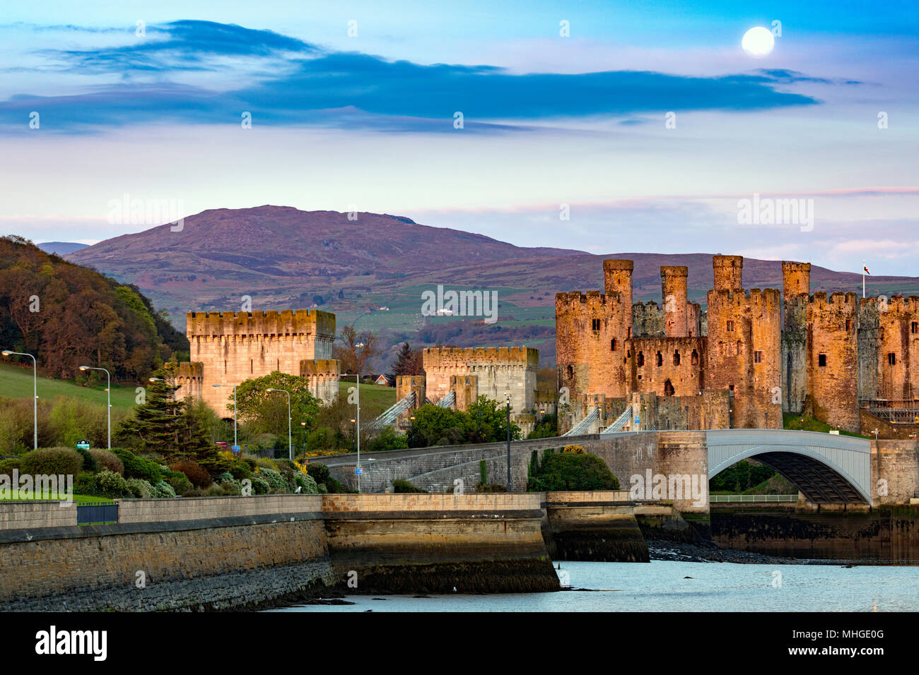 A beautiful sunrise dawn and setting moon over Conwy Castle and Carnedd Llewelyn and the start of Snowdonia National Park, Cowny, Wales, UK Stock Photo