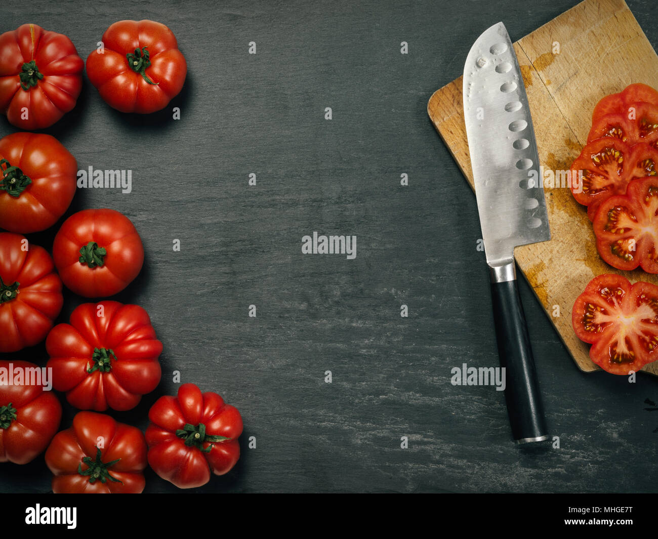 Photo of a table top with Marmande tomatoes, a knife, and slices on a cutting board. Stock Photo
