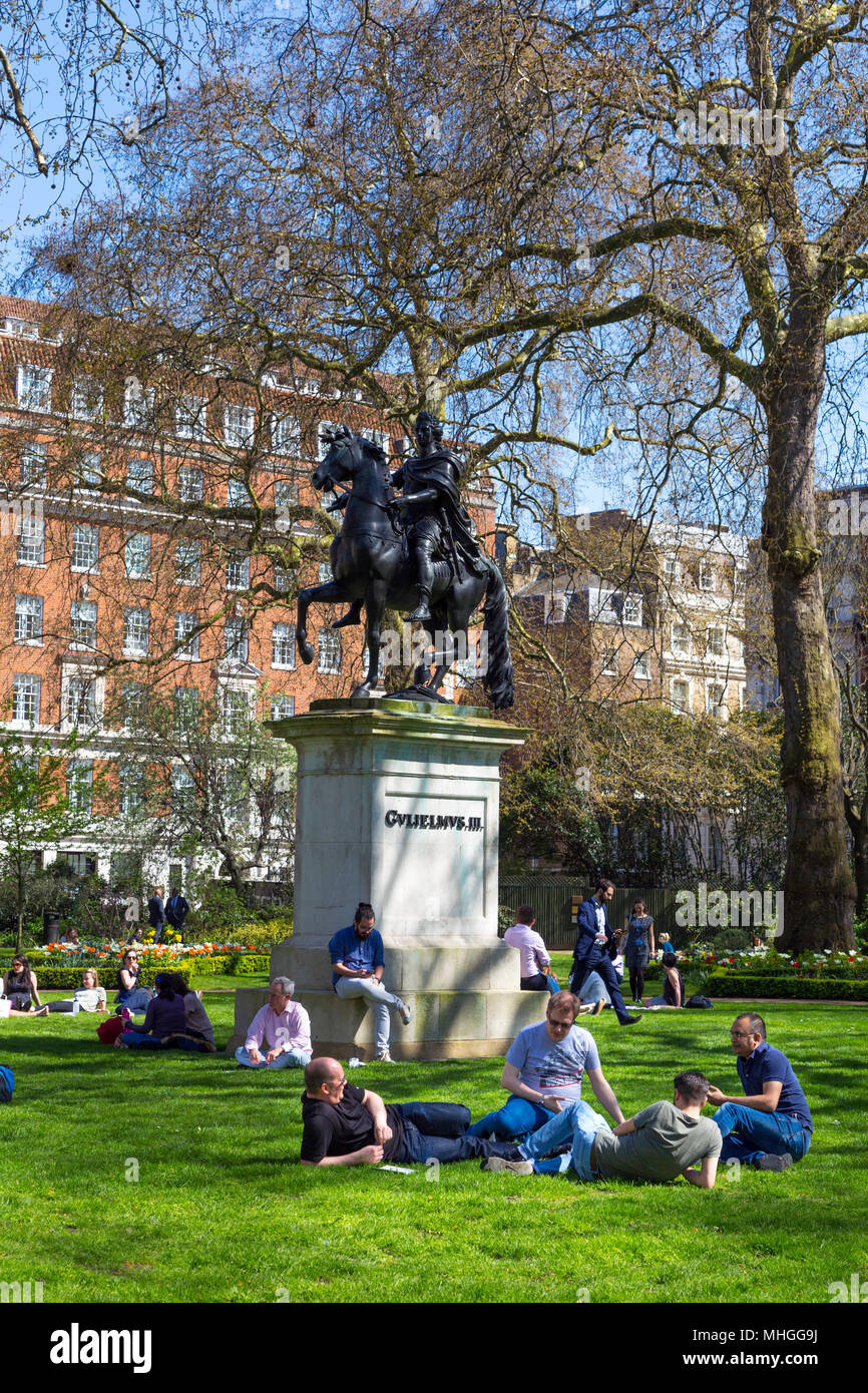 People sitting on the grass and eating lunch in a small city park, St James's Square Garden, London, UK Stock Photo