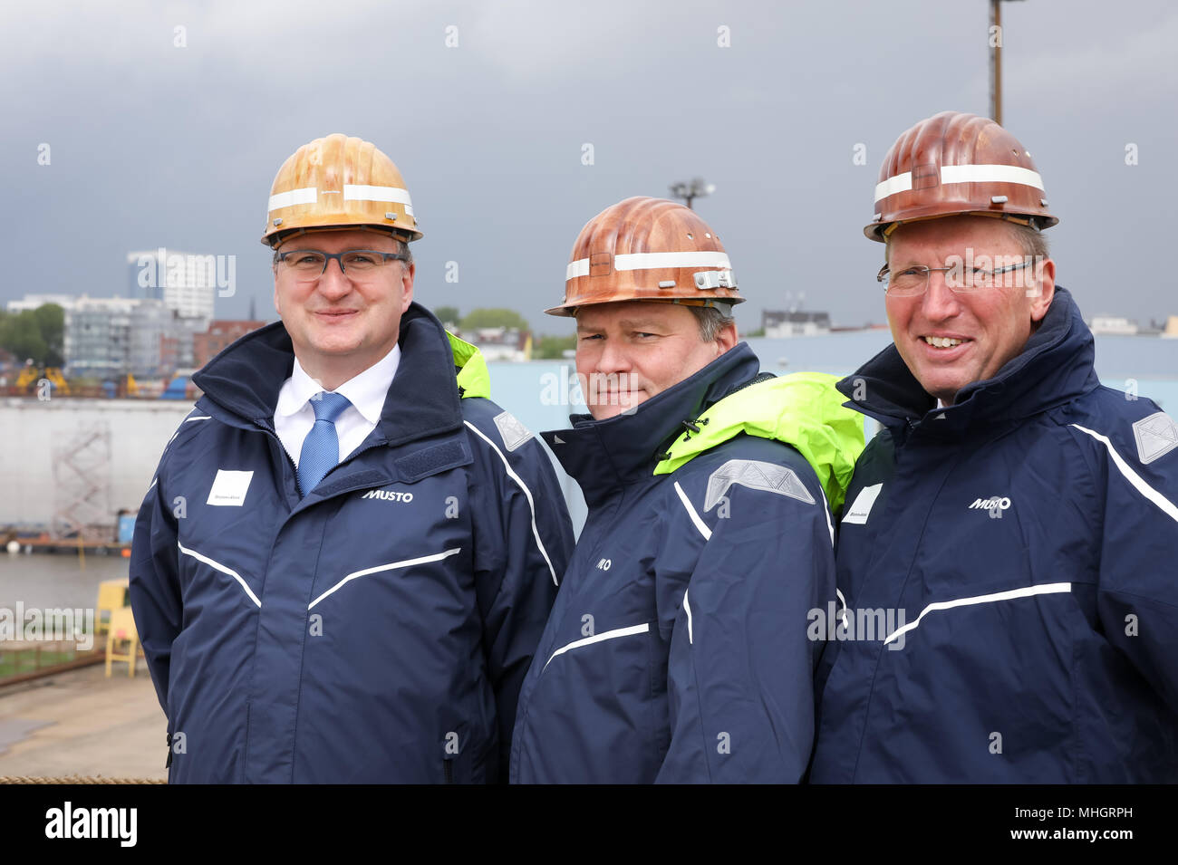 26 April 2018, Germany, Hamburg: Ralph Petersen (L) and Dieter Dehlke, CEO of Blohm Voss, and Chairman of the Supervisory Board and director of technology at Luerssen, Klaus Borgschulte (R), standing on a podium in front of the cruise ship 'Brilliance of the Seas' by the shipping company Royal Caribbean International im Schwimmdock Elbe 17 on the grounds of the shipyard of Blohm Voss. The traditional shipyard is on a new course after having been taken over by the Luerssen-Gruppe of Bremen one and a half years ago. Photo: Christian Charisius/dpa Stock Photo