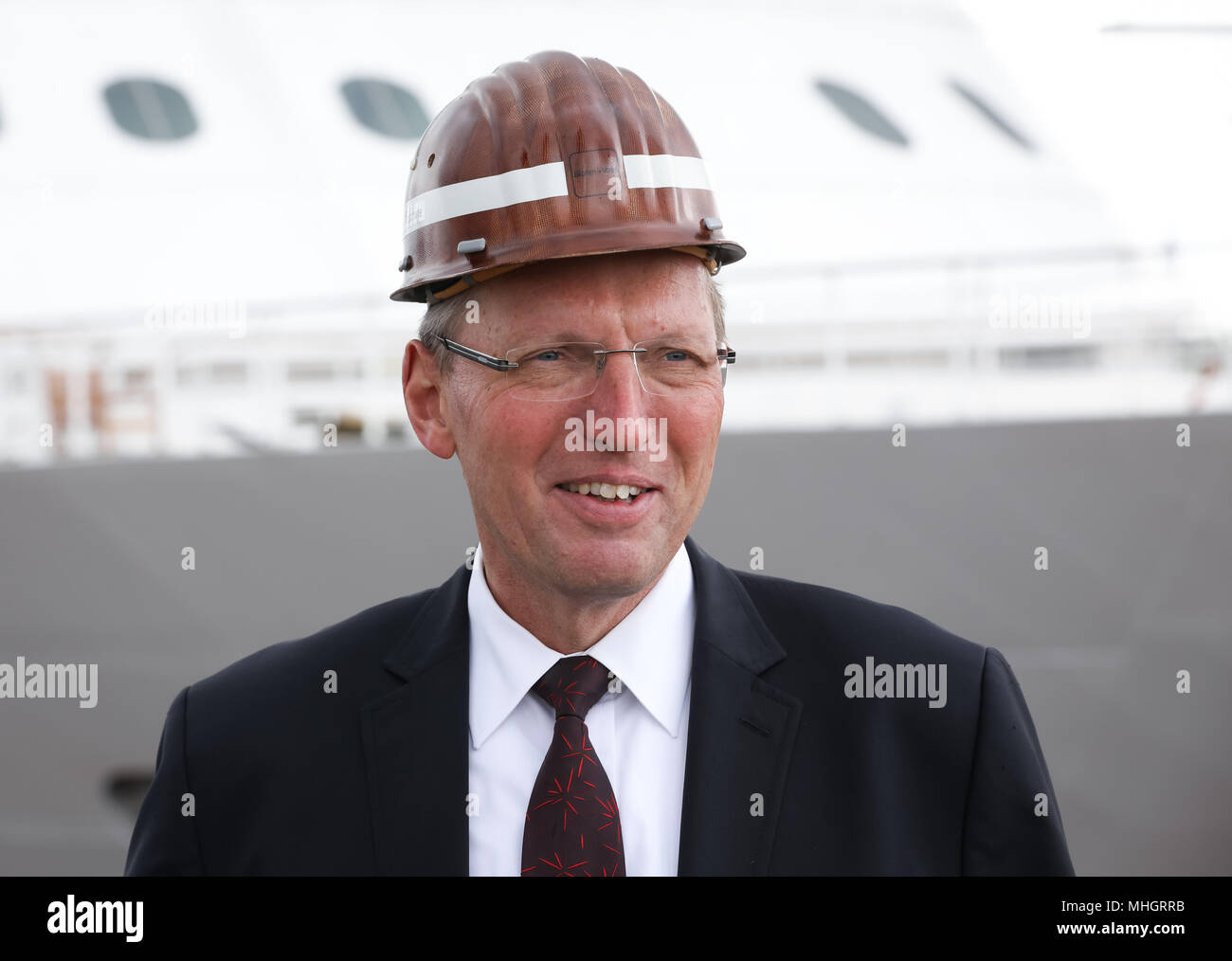 26 April 2018, Germany, Hamburg: Chairman of the Supervisory Board and director of technology at Luerssen, Klaus Borgschulte, standing on a podium in front of the cruise ship 'Brilliance of the Seas' by the shipping company Royal Caribbean International im Schwimmdock Elbe 17 on the grounds of the shipyard of Blohm Voss. The traditional shipyard is on a new course after having been taken over by the Luerssen-Gruppe of Bremen one and a half years ago. Photo: Christian Charisius/dpa Stock Photo