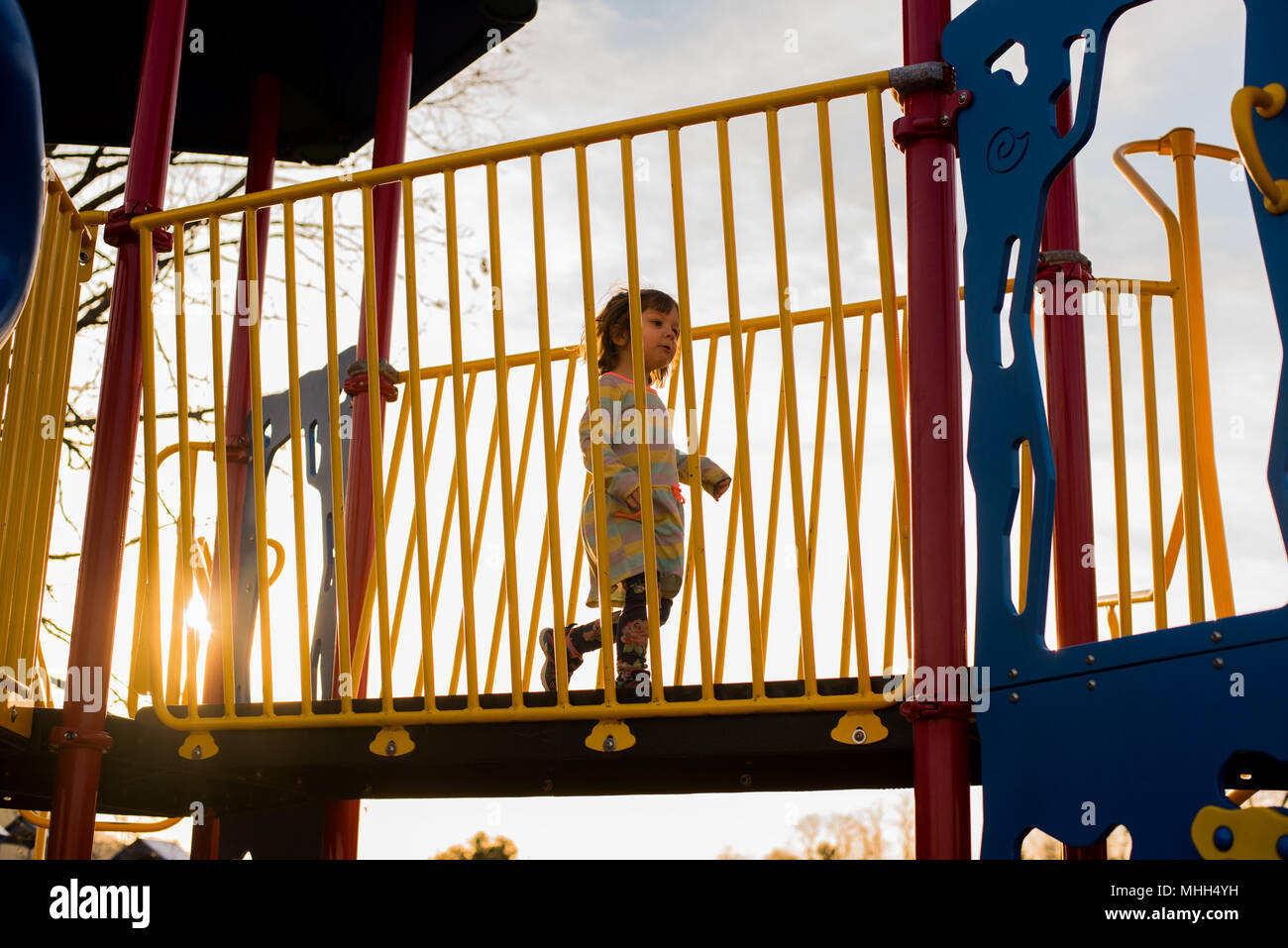 A toddler girl runs across playground equipment on a sunny day. Stock Photo