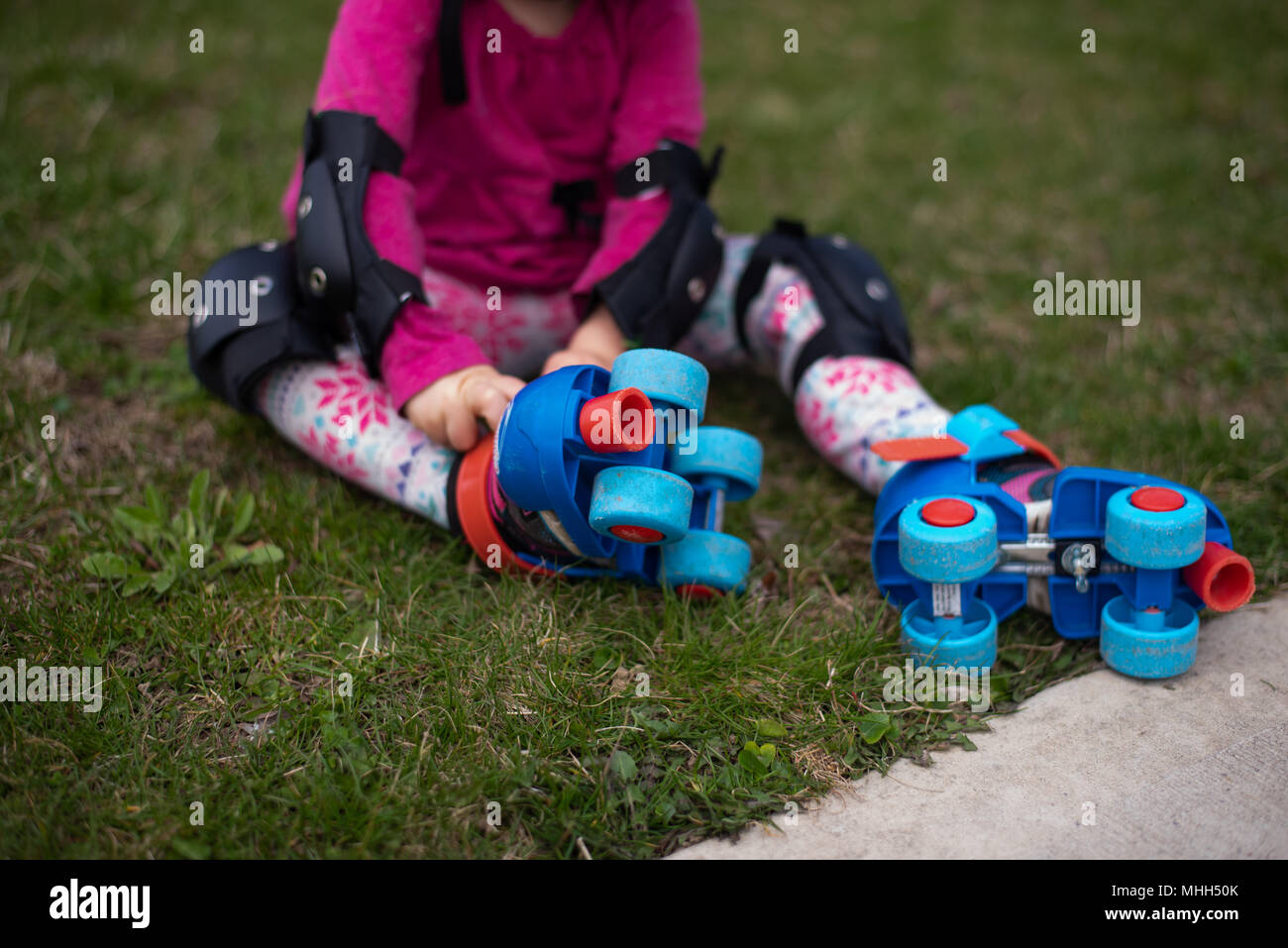 toddler girl wearing knee and elbow pads putting skates on Stock Photo Alamy