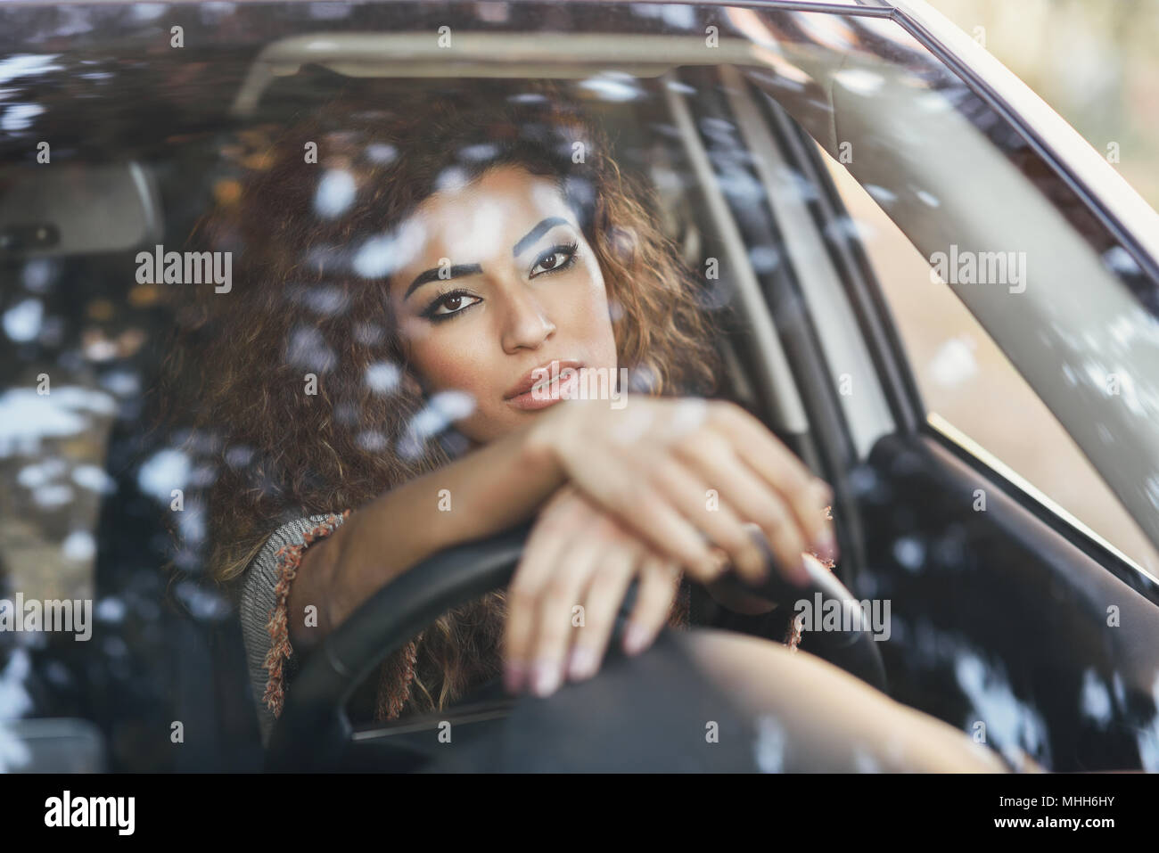 Beautiful young arabic woman inside a nice white car looking through the window. Arab girl wearing casual clothes. Stock Photo