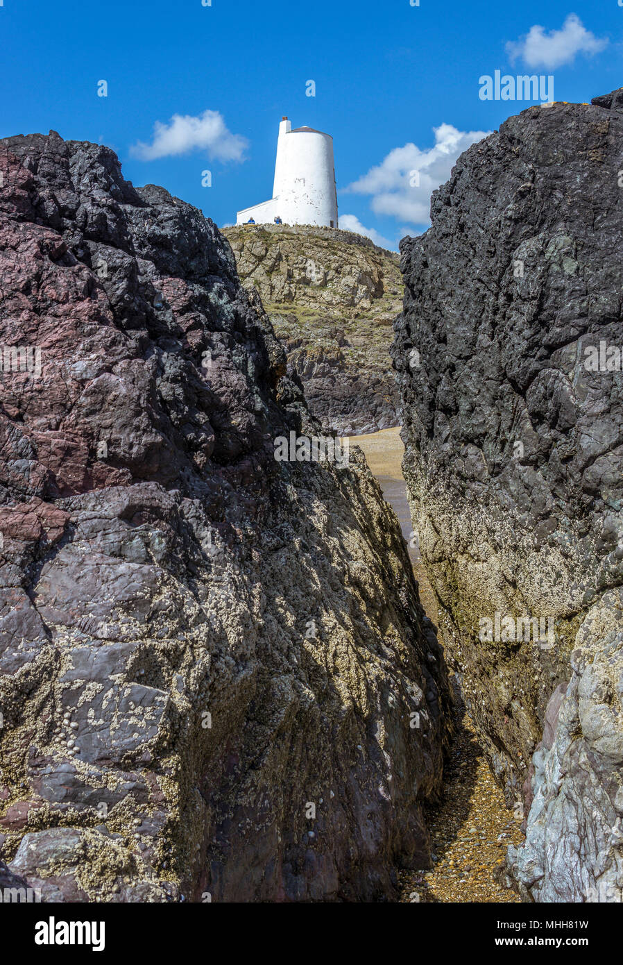 A view of Twr Mawr Lighthouse on Llanddwyn Island, Anglesey, North Wales through a gap in the volcanic lava pillars. Stock Photo