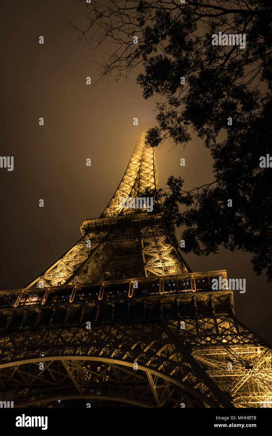 The Eiffel Tower at night with its summit in the fog / mist / clouds Stock Photo