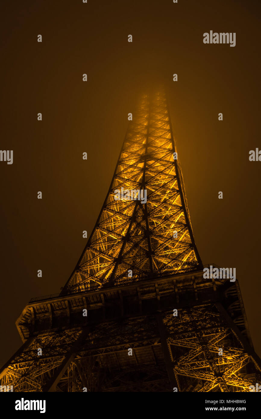 The Eiffel Tower at night with its summit in the fog / mist / clouds Stock Photo