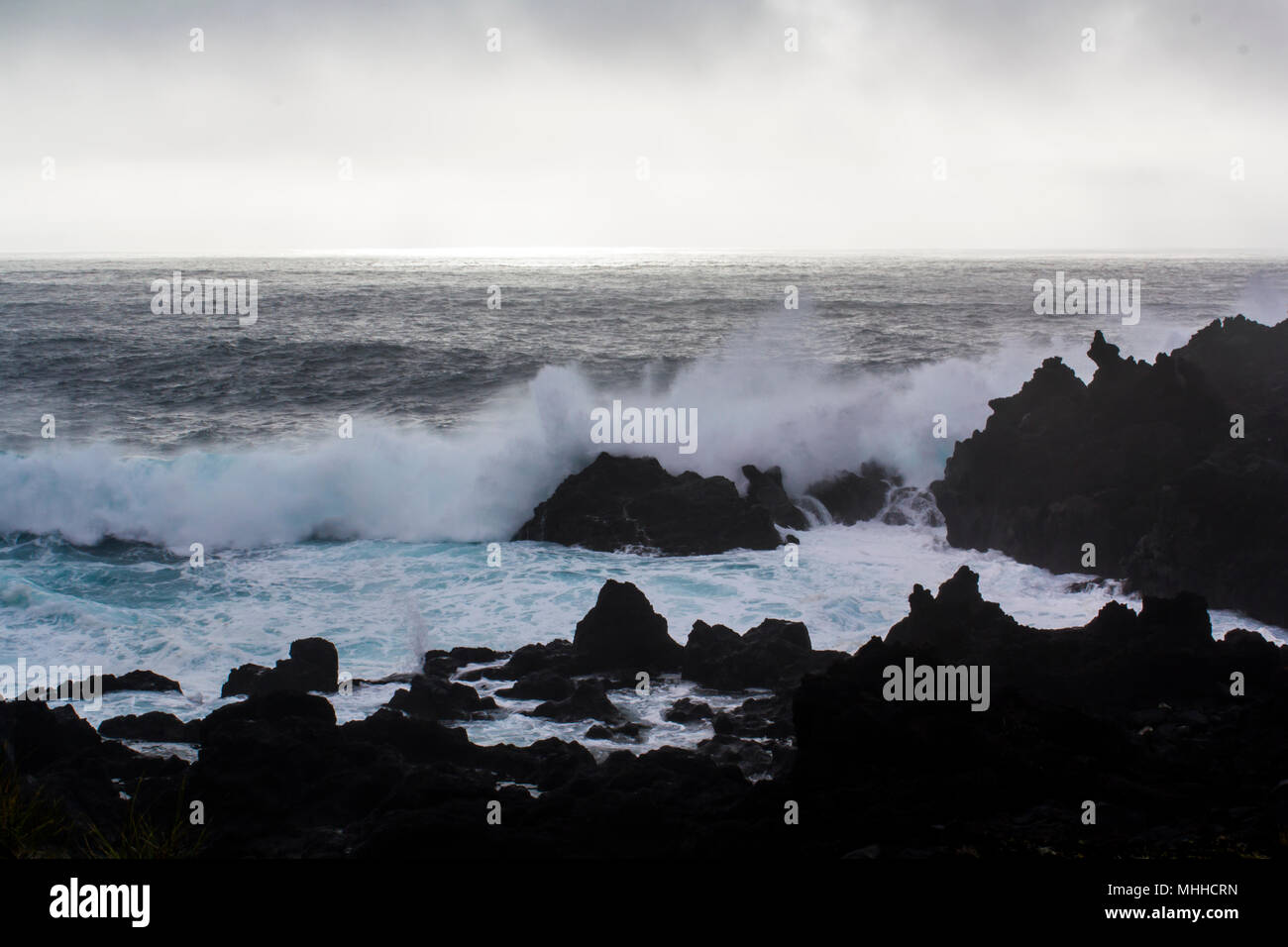 Waves crashing against black volcanic rock formations Stock Photo