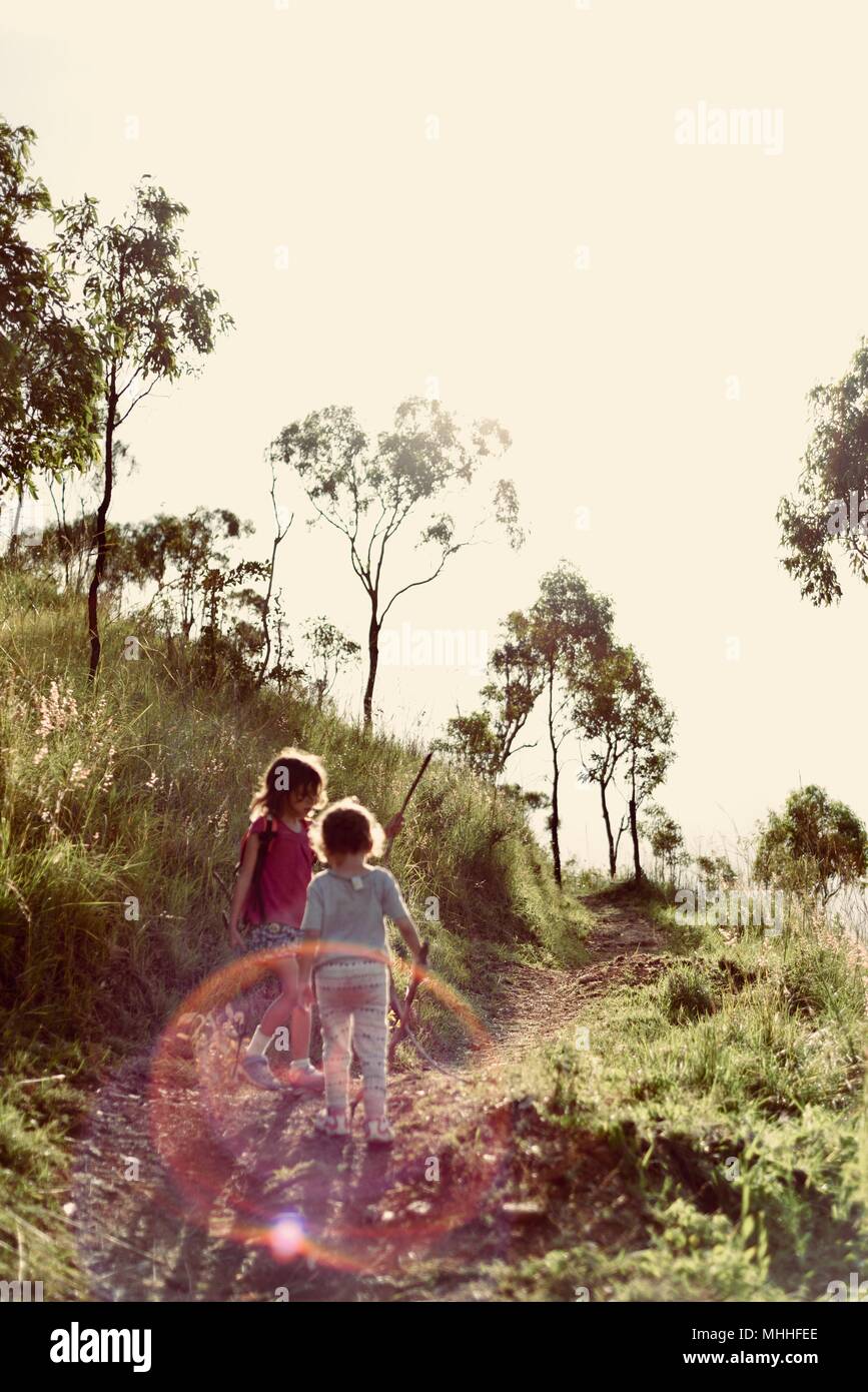 Two children playing on a gravel path in a forest in a vintage backlit scene, Mount Stuart hiking trails, Townsville, Queensland, Australia Stock Photo