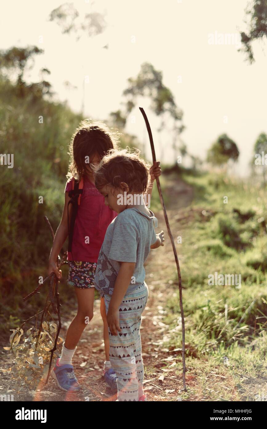 Two children playing on a gravel path in a forest in a vintage backlit scene, Mount Stuart hiking trails, Townsville, Queensland, Australia Stock Photo